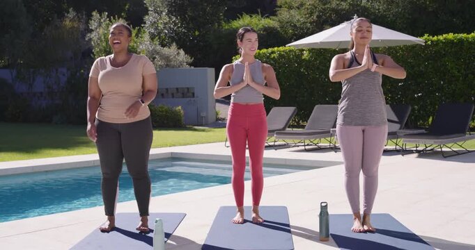 Three female friends following instructor cue doing warmup lunges on poolside patio with yoga mats
