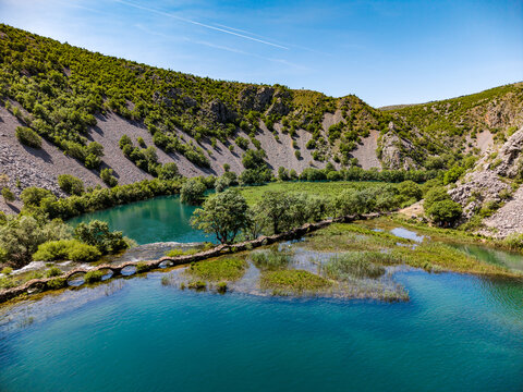 Aerial view of Kudin most na Krupi stone bridge crossing the turquoise Krupa river canyon with lush green vegetation and rocky slopes Golubic, Zadarska zupanija, Croatia.