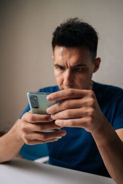 Vertical portrait of handsome male using typing smartphone at wooden desk, focusing intently on digital screen, representing contemporary mobile communication and technology lifestyle.