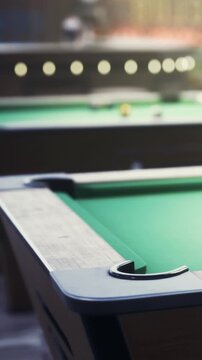 People gather at a bar in the evening to play pool. The green tables stand out in the setting. Players focus on their shots while enjoying the atmosphere.