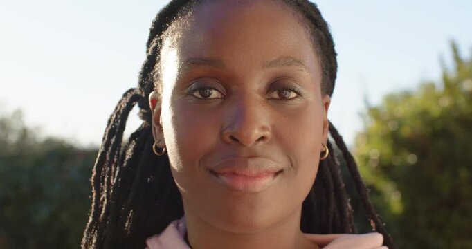 African American woman closing eyes then reopening, smiling and laughing in garden in pink hoodie