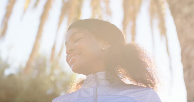 Adult African American woman noticing camera turning lowering gaze smiling in park wearing jacket