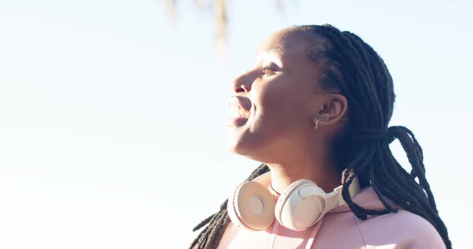 African American women holding smartphone and headphones, calling out to attract friend at park