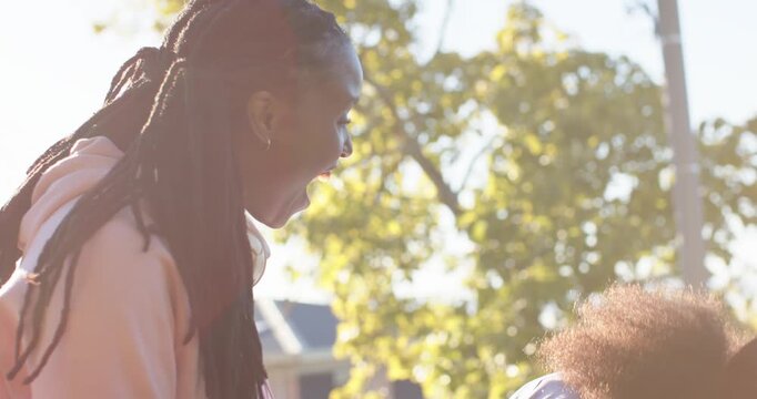 African female friends leaning together spotting funny content on smartphone, laughing on sidewalk