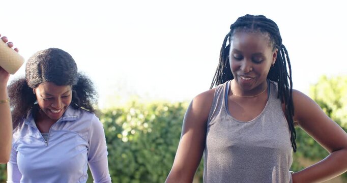 African American friends patting shoulder at backyard while man entering sipping bottle, hydrating