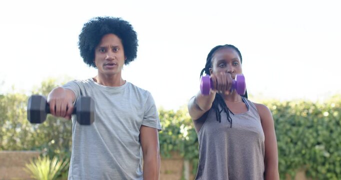 African American friends in gray tops starting lifting black purple weights for fitness in garden