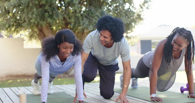 Trainer kneeling on deck, giving corrective cues to two women planking on green mats in sportswear