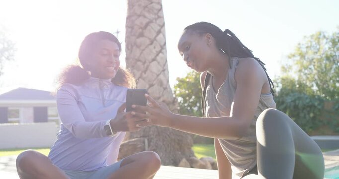 African American women in gymwear sitting deck sharing smartphone one showing screen other tapping