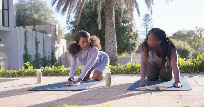 Female friends kneeling on yoga mats on patio, left woman cueing stretches, both warming up