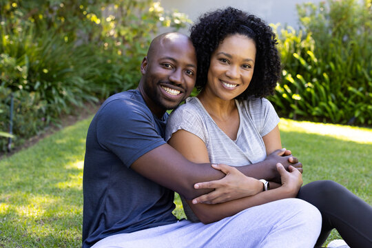African American couple sitting on lawn hugging, showing wristwatch and wearing athletic clothing