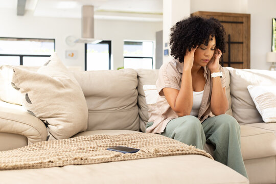 African American woman sitting at home wearing beige top holding head smartphone nearby, copy space