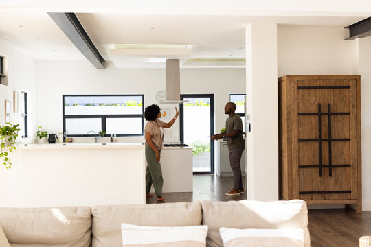 African American couple standing and pointing at stainless-steel hood by kitchen island, kettle