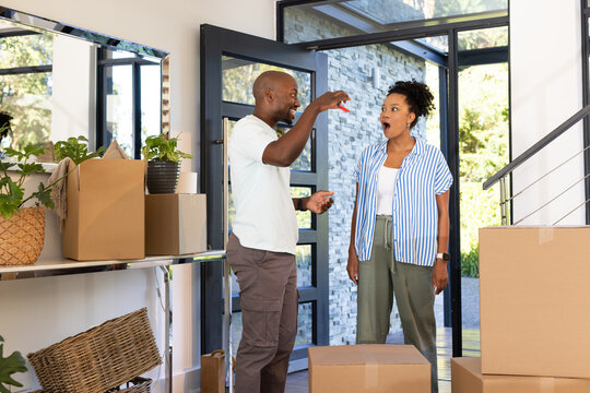 African American couple standing in foyer surrounded by packed moving boxes while man offering keys