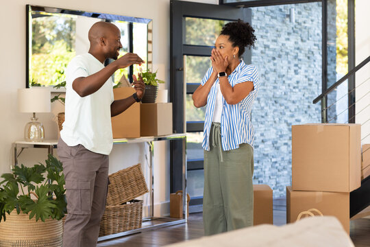 African American couple standing among moving boxes in entry, man gesturing, woman covering mouth