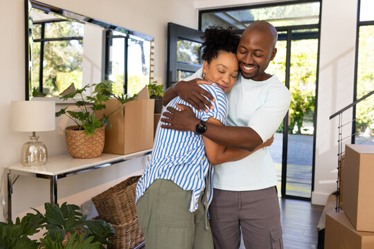 African American couple hugging while unpacking near front glass door with boxes and mirror