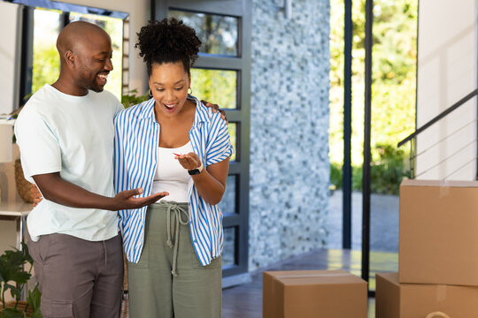 African American couple smiling, standing in modern entry holding key near stacked moving boxes