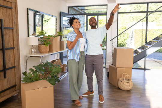 African American couple standing and pointing in entry with moving boxes, plants and glass windows