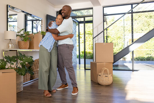 African American couple embracing in modern home entry among moving boxes by console table