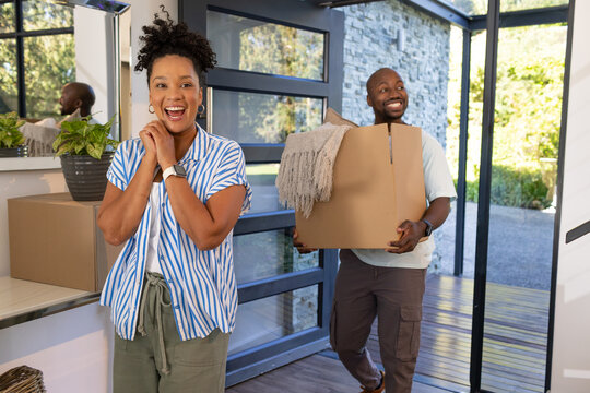 African American couple arriving at front entryway carrying cardboard boxes with throw blanket