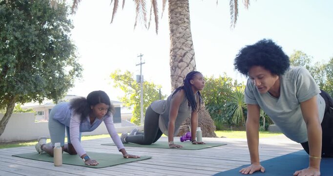 African American instructor guiding women from child's pose into cobra on deck mats, aligning neck