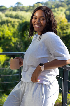 Woman standing on deck holding tan ceramic mug, smartwatch on wrist, wearing gray sweats