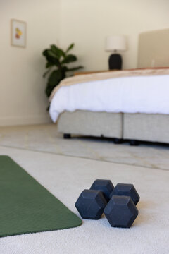 Black hex dumbbells are resting on light carpet near green mat beside bed and lamp