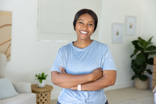 Adult African woman standing arms crossed at home wearing light blue T-shirt and fitness tracker