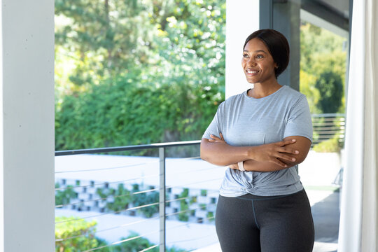 African woman standing on balcony, in knotted tee and leggings, showing fitness tracker, copy space
