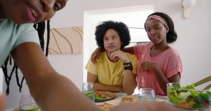 African American women adjusting camera at home table, stepping in and sharing pizza and salad