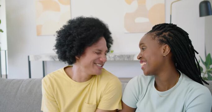 African American friends sharing hug on sofa, yellow shirt, pink friend entering, smiling at camera