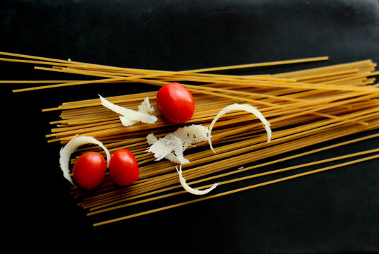  Raw spaghetti with cherry tomatoes and parmesan cheese on a black background. Minimalist food composition with dramatic lighting, highlighting textures and natural colors.