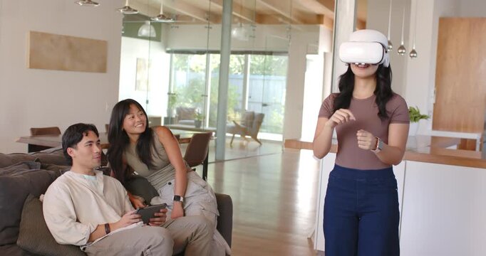 Diverse friends at home watching woman wearing white VR headset showing as man testing tablet VR
