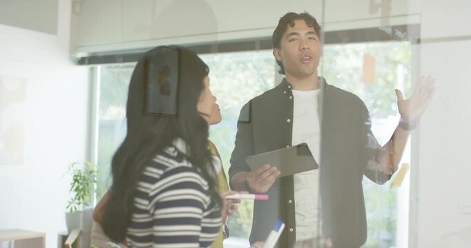 Diverse coworkers presenting from tablet notes, using markers on glass whiteboard, finalizing plan