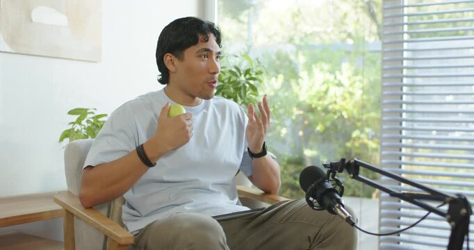 African American man answering offscreen prompt, speaking and holding green apple near window mic