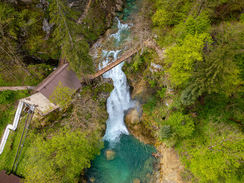 Aerial view of Slap Sum waterfall with a wooden bridge and lush green forest in Zgornja Besnica, Kranj, Slovenia.