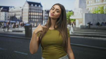 Fototapeta premium Woman points thumb to chest on a busy street in front of city buildings with a direct gaze at camera; confidence self identity.