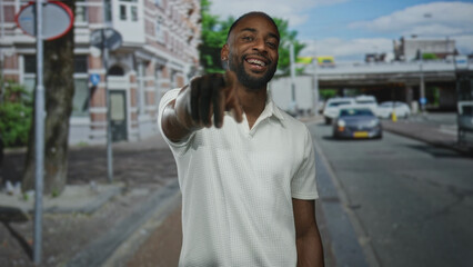 Obraz premium Man points finger and smiles on street wearing white polo and leather glove showing braces and forearm; confidence invitation.