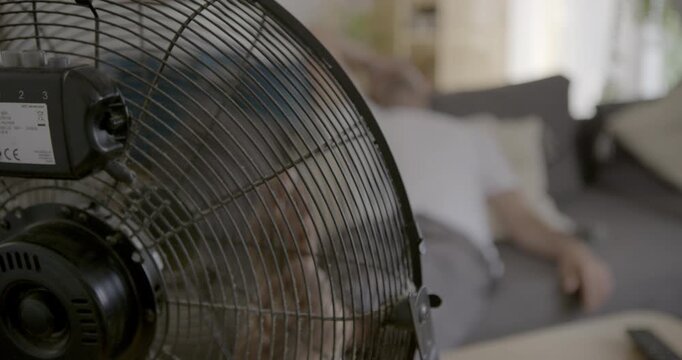Cooling Breeze: A powerful electric fan circulates air, providing a welcome respite from the heat for a person relaxing on a sofa.