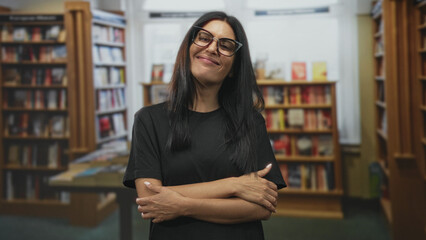 Woman arms crossed smiling in front of bookshelves in a bookstore inside a building  serene confidence. © Krakenimages.com