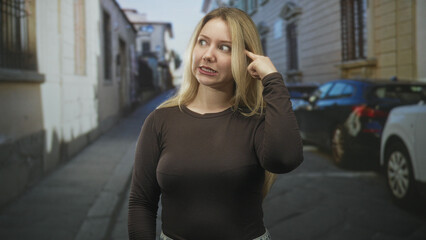 Fototapeta premium Woman pointing finger to temple on street near parked cars and buildings, showing a thinking gesture and puzzled expression; confusion.