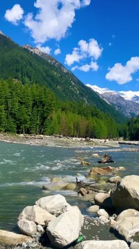 Beautiful mountain river flowing through pine forest with snow-covered peaks under blue sky, scenic landscape of Kumrat Valley Pakistan.