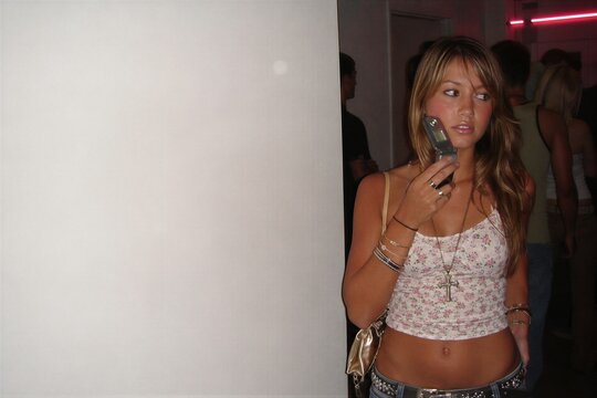 Woman talking on retro flip phone at party. Y2K fashion style with floral camisole, jewelry and low rise jeans. Nostalgic 2000s tech aesthetic and social lifestyle snapshot