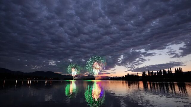 Colorful fireworks display over calm lake at night. Spectacular celebration illuminates sky and reflects on water. Joyful atmosphere creates memorable moments for viewers.
