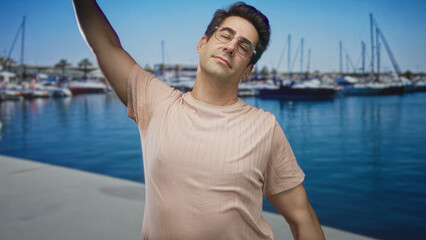 Fototapeta premium Man stretching arms with eyes closed by a marina dock and boats near a street; relaxation contentment.