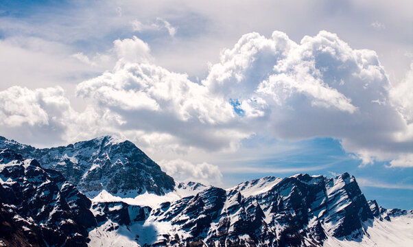 Aerial view of the snow-capped mountain peaks and rugged rocky ridges under dramatic white clouds near Thalkirch in Safiental, Graubunden, Switzerland.