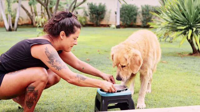 Tattooed woman feeding golden retriever a BARF diet outdoors