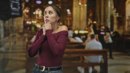 Fototapeta premium Woman with clasped hands at chest and closed eyes in ornate cathedral building; prayerful contemplation.