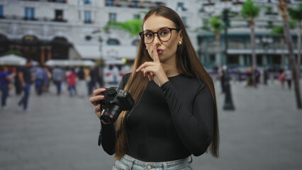 Fototapeta premium Woman holding dslr camera with hands checking settings on street while smiling and wearing glasses, reviewing images on the display; curiosity interest.