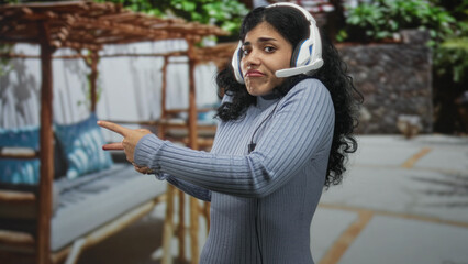 Fototapeta premium Woman young brunette wearing headset pointing finger on street near outdoor patio seating and pergola; skeptical expression.