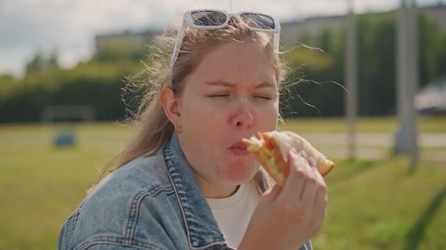 White woman in denim eating pastry with playful messy bite, crumbs flying, sunglasses on head, summer park background, candid expressions, chewing and thoughtful pause, casual picnic vibe, warm